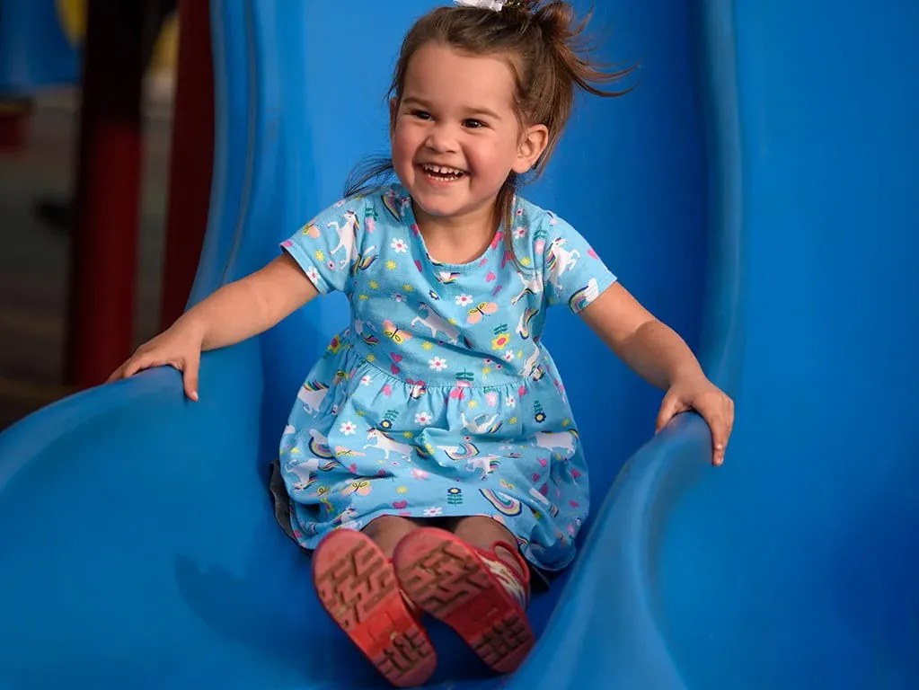 Smiling girl coming down a blue slide